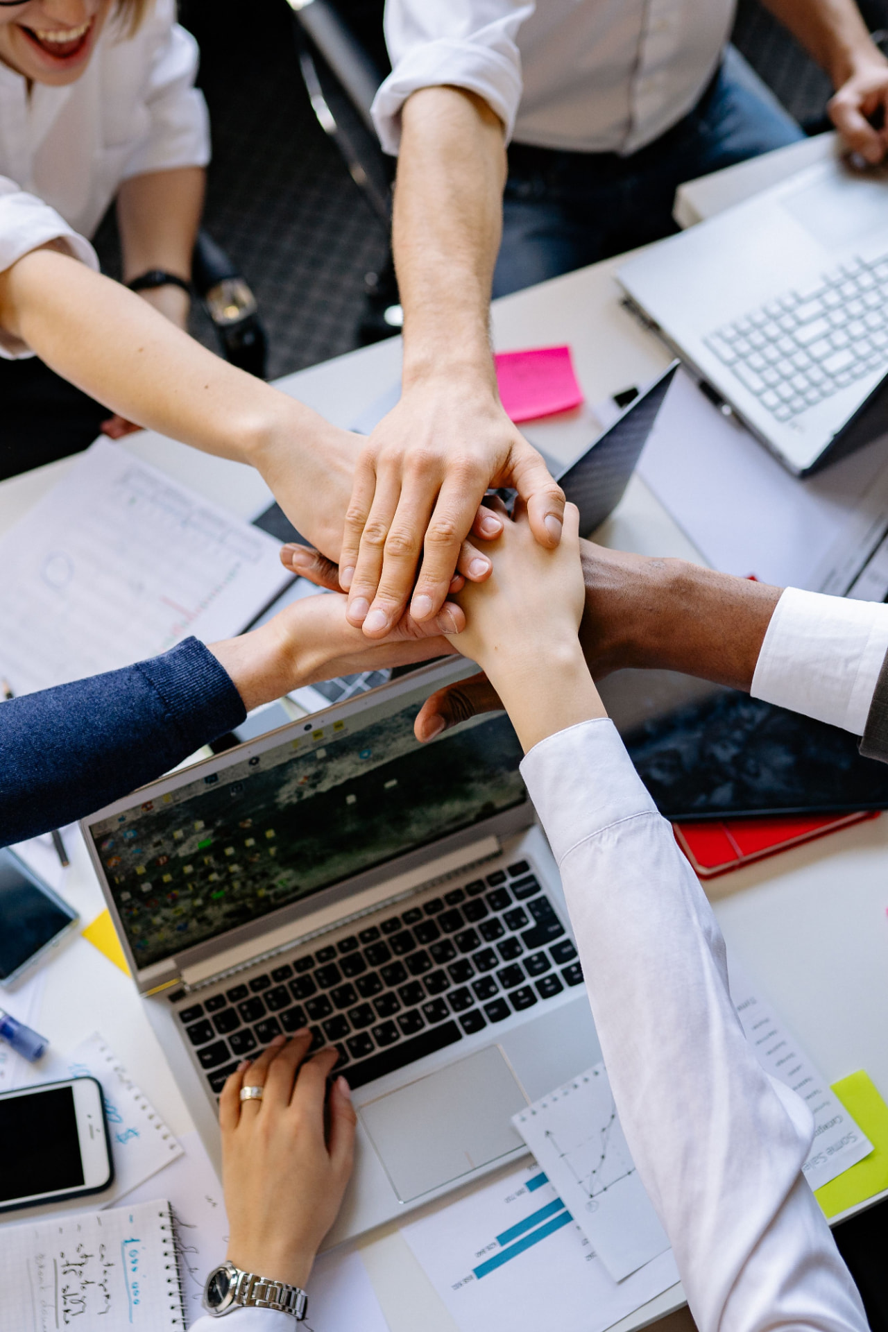 Manos de equipo unidas sobre un laptop en una mesa de trabajo